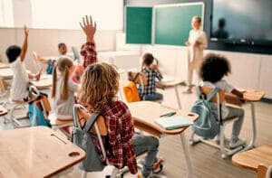 Children in room participating with teacher and raising hands